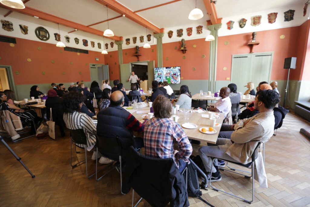 Attendees sitting at tables during an event in Toynbee Hall's Ashbee Hall.